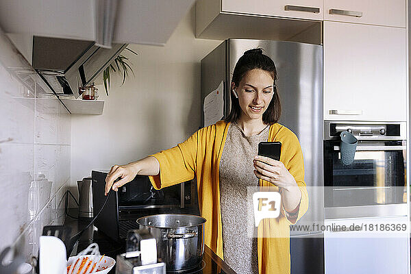 Frau kocht und führt Videoanrufe per Smartphone in der Küche