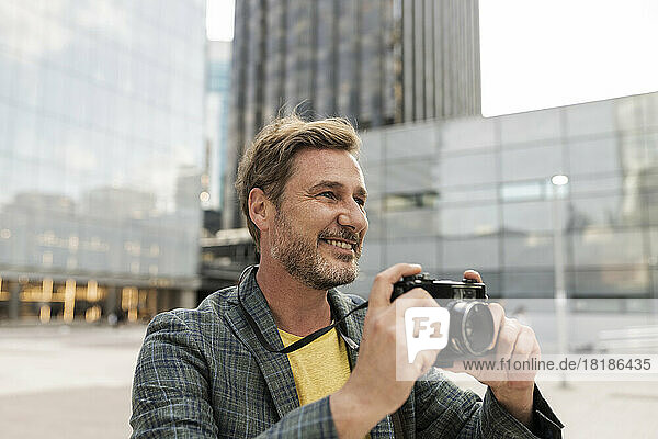 Smiling man taking photos through camera in city