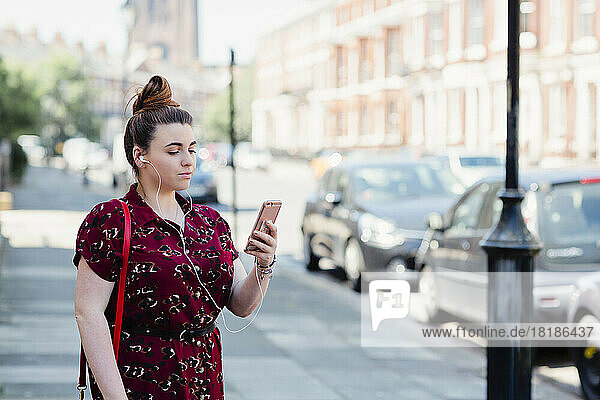 Portrait of woman with earphones standing on pavement looking at cell phone  Liverpool  UK