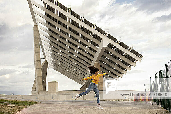 Happy young woman with arms outstretched enjoying in front of solar panels
