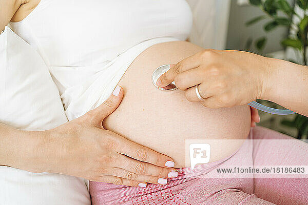 Hand of doctor examining pregnant woman belly with stethoscope