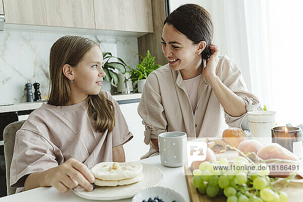 Happy woman talking with daughter at dining table in kitchen