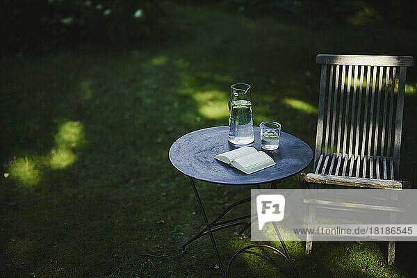 Open book and glass of water on table with chair in garden
