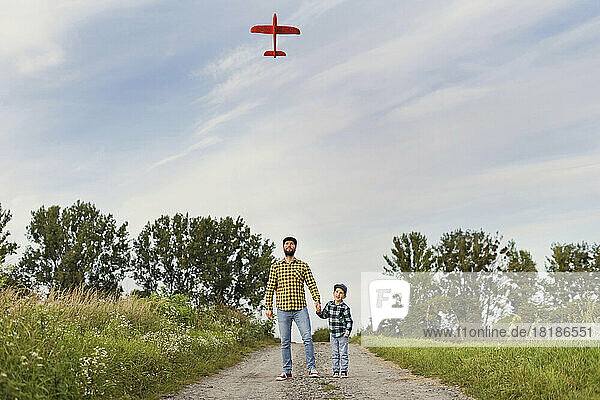 Father and son looking at model airplane together on dirt road