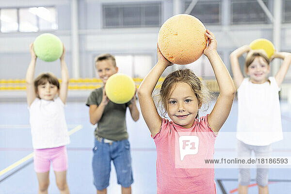 Smiling girl holding ball at school sports court with friends in background