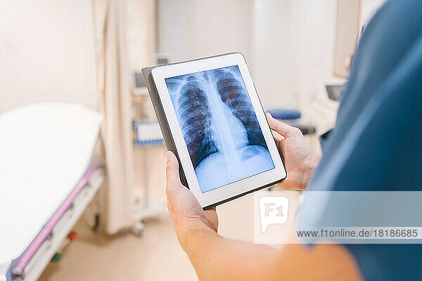 Hands of doctor holding tablet PC and examining x-ray image at hospital