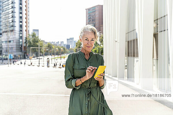 Mature woman with smart phone on footpath in city