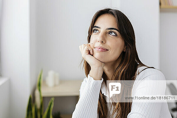Thoughtful smiling woman with hand on chin at home