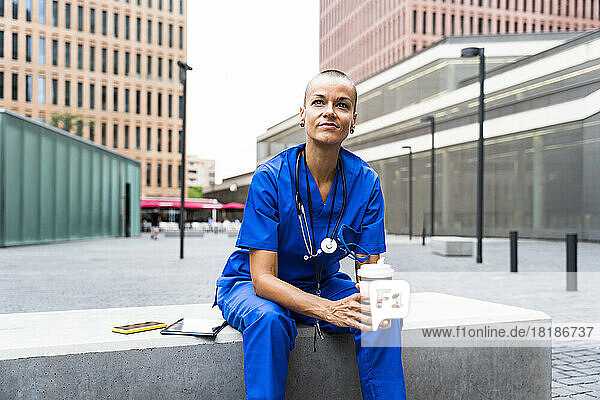 Thoughtful healthcare worker holding coffee cup sitting on bench