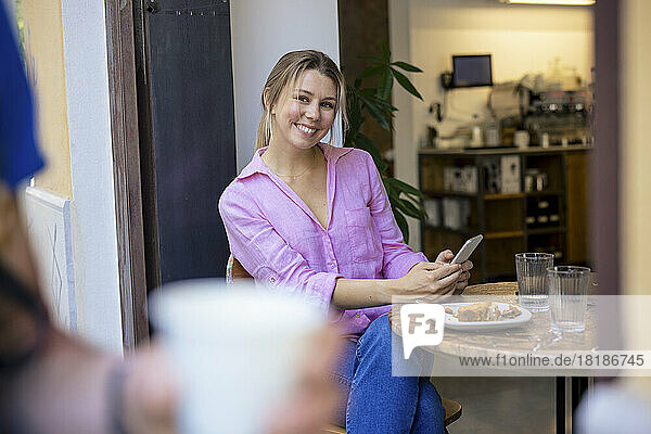 Happy blond businesswoman sitting with smart phone at table in cafe