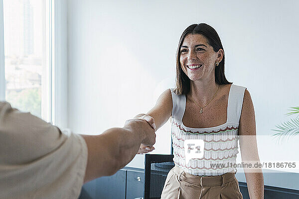 Happy real estate agent shaking hands with client in office
