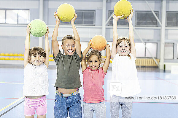 Fröhliche Schüler mit erhobenen Armen halten den Ball zusammen und stehen auf dem Schulsportplatz