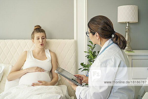 Arzt spricht zu Hause mit schwangerer Frau im Bett