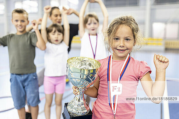 Mädchen mit Medaille und Trophäe feiert Sieg mit Freunden auf dem Schulsportplatz