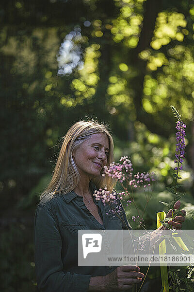 Smiling mature woman touching flowering plants in garden