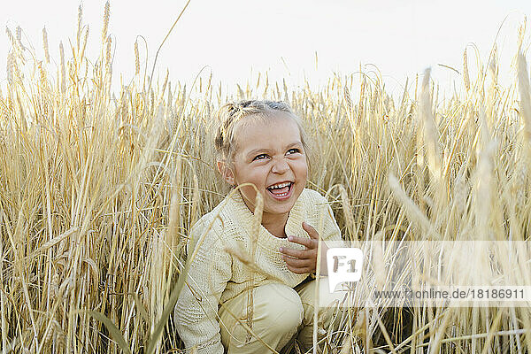 Cheerful girl crouching amidst crops at field