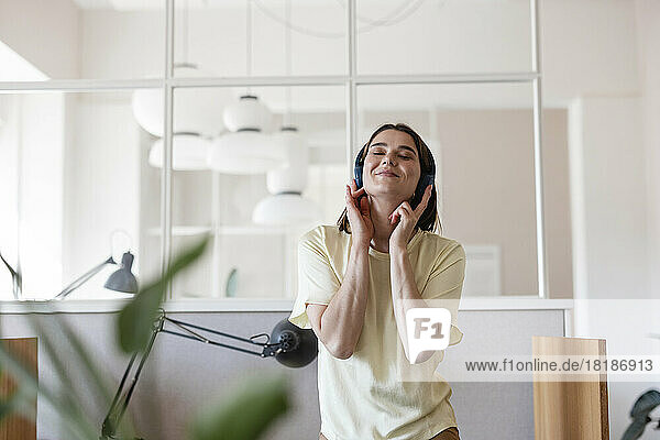 Businesswoman with eyes closed enjoying music listening through wireless headphones in office