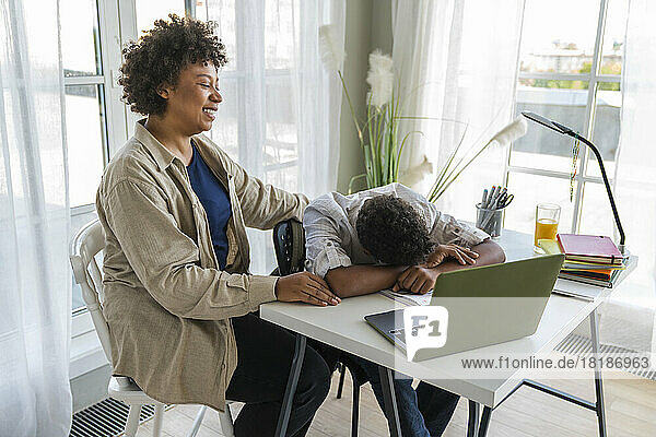Mother sitting by son resting head on table at home