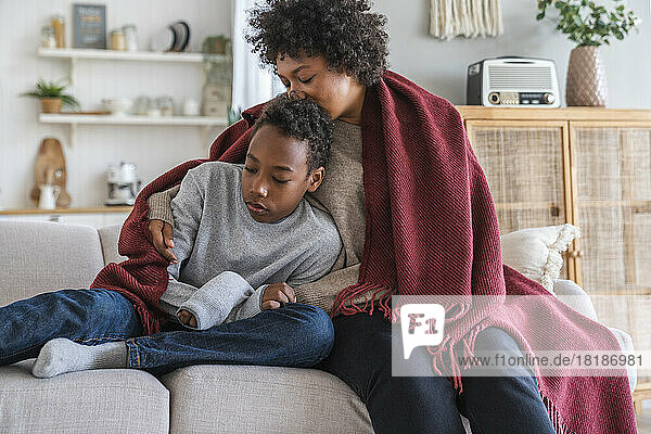 Mutter küsst Sohn mit eingewickelter Decke zu Hause auf den Kopf