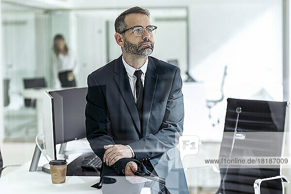 Contemplative businessman sitting with tablet PC in office
