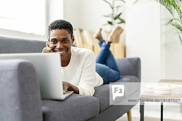 Smiling woman lying on couch using laptop