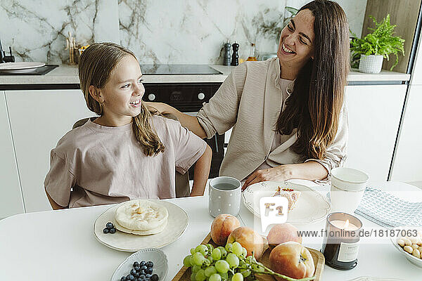 Happy woman with daughter at dining table in kitchen