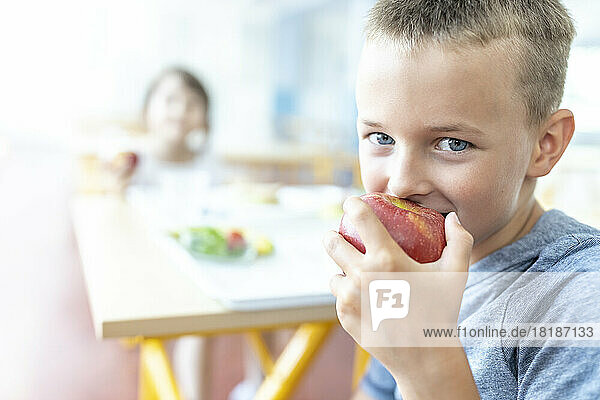 Schoolboy eating fresh apple at lunch break in cafeteria