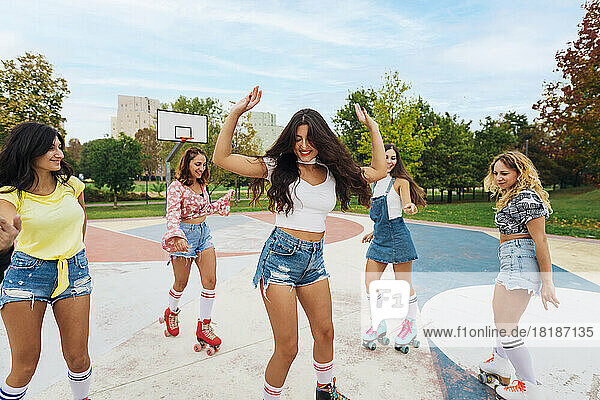 Carefree woman with friends dancing in roller skates at sports court