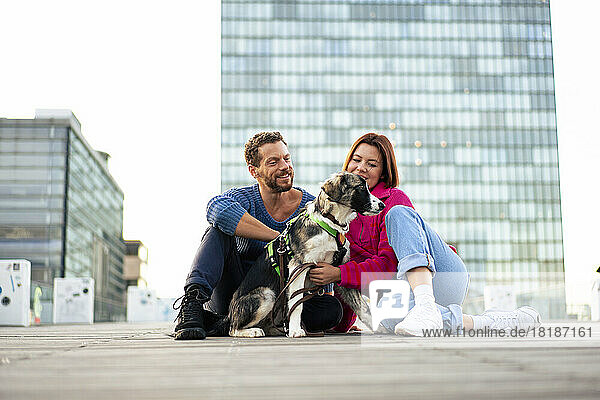 Happy couple spending leisure time with dog sitting on road in front of building