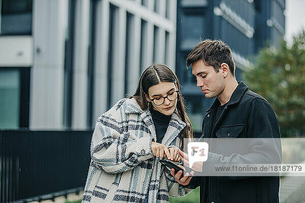 Young man and woman talking over mobile phone on street