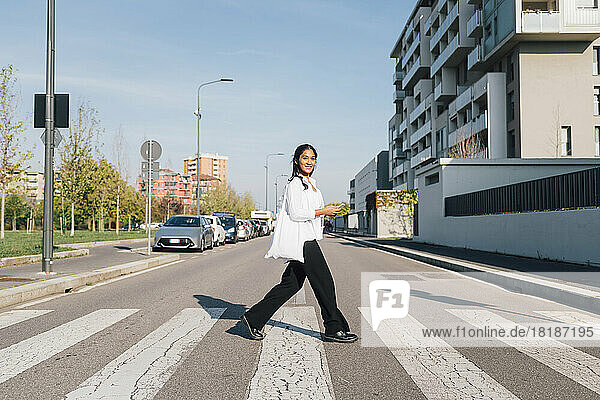 Lächelnde Frau überquert an einem sonnigen Tag die Straße