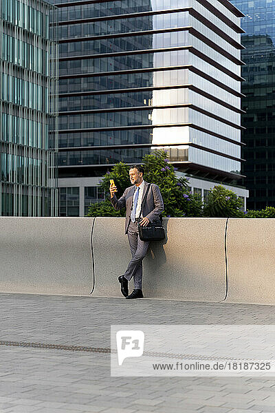 Businessman using smart phone leaning on wall