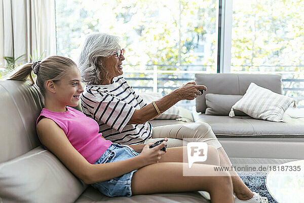 Grandmother and granddaughter spending leisure time playing video game on sofa at home