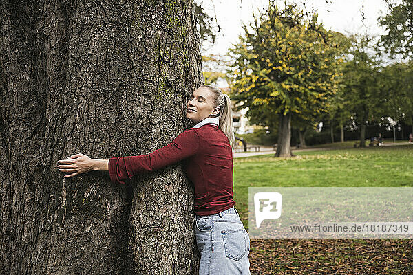 Smiling woman hugging tree at park