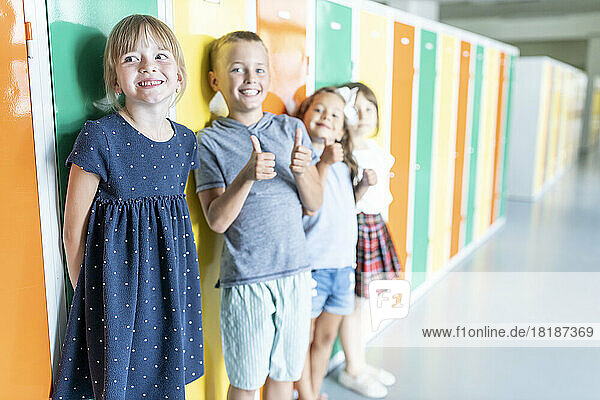 Happy elementary students standing near colorful lockers in school corridor