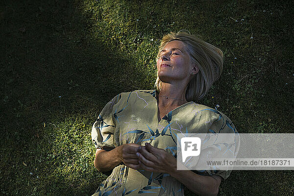 Reife Frau liegt mit geschlossenen Augen im Garten auf Gras