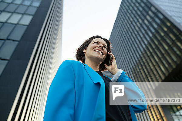Glückliche Geschäftsfrau  die am Bürogebäude steht und mit dem Mobiltelefon spricht