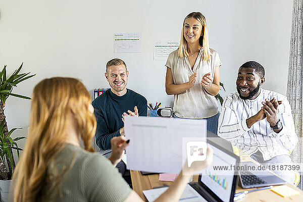 Businesswoman showing document to smiling colleagues clapping hands in meeting