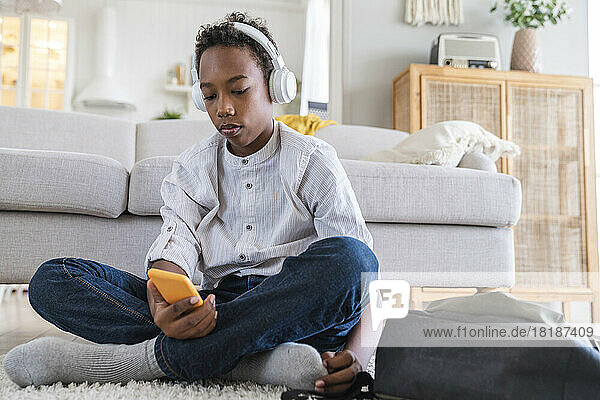 Boy wearing headphones listening to music sitting with mobile phone at home
