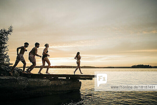 Männliche und weibliche Freunde laufen im Urlaub bei Sonnenuntergang auf dem Steg Richtung See
