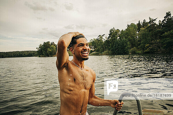 Glücklicher Mann ohne Hemd mit Kopf in der Hand beim Schwimmen im See während des Urlaubs