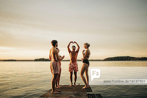 Freunde betrachten einen Mann  der auf einem Steg am See steht und gestikuliert