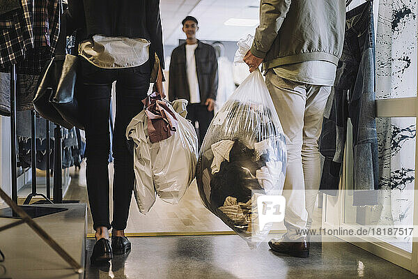 Niedriger Ausschnitt von männlichen und weiblichen Modedesignern  die bei einem Workshop eine Plastiktüte mit recycelter Kleidung halten