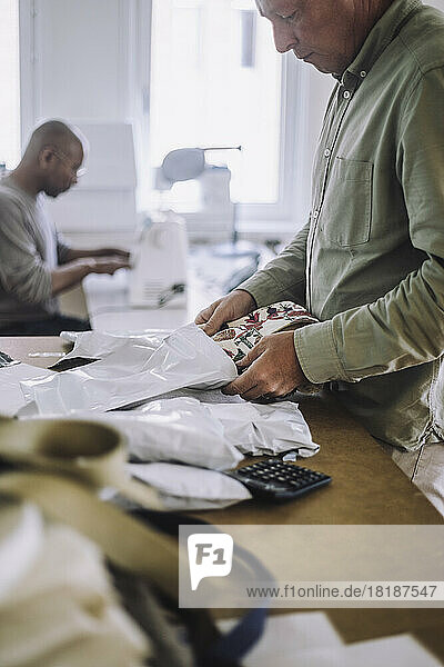 Männlicher Modedesigner beim Verpacken von Stoffen während der Arbeit im Atelier