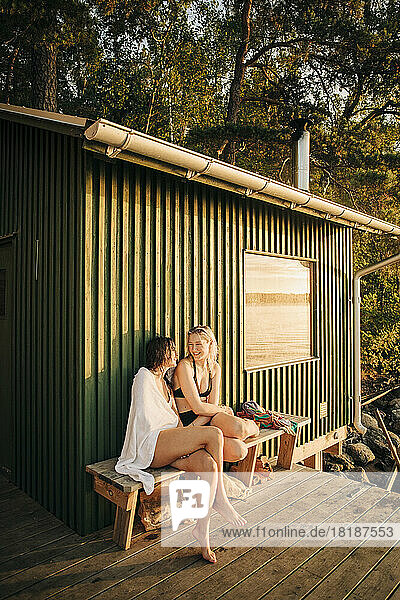 Freundinnen sitzen bei Sonnenuntergang auf einer Bank in der Nähe einer Hütte