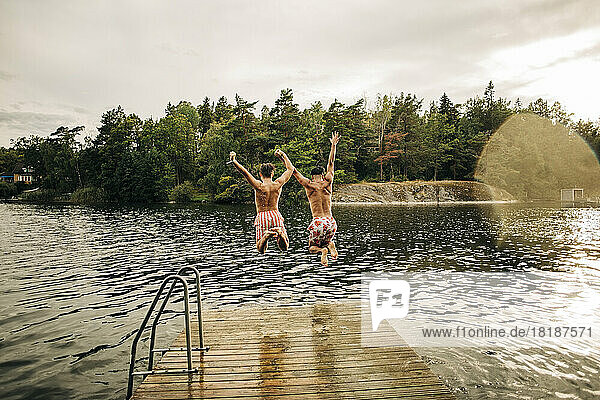 Carefree male friends with arms raised jumping in lake during vacation