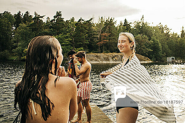 Smiling woman wearing towel while looking at female friend during vacation