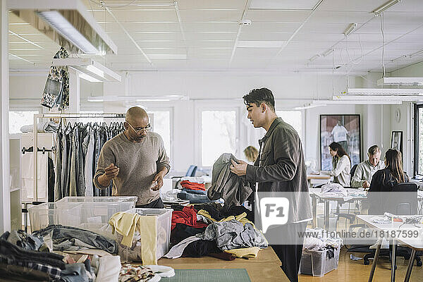 Male fashion designers discussing with each other while sorting recycled clothes at workshop