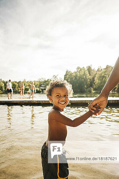 Seitenansicht eines aufgeregten Jungen  der die Hand seiner Mutter hält  während er am See steht