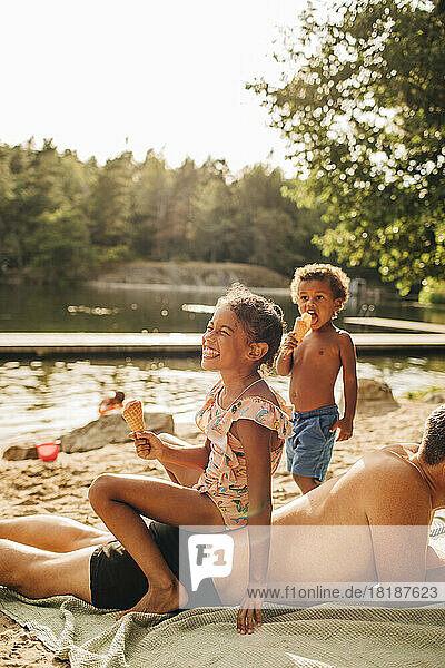 Lächelndes Mädchen mit Eis auf dem Rücken des Vaters im Urlaub